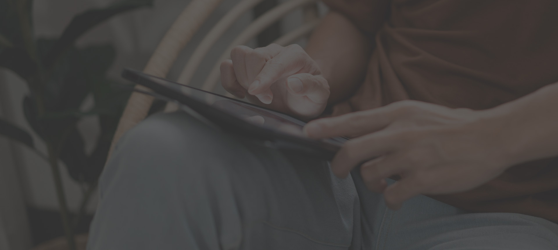 male with his casual T shirt and jeans sitting comfortably on the wooden chair and doing touchscreen